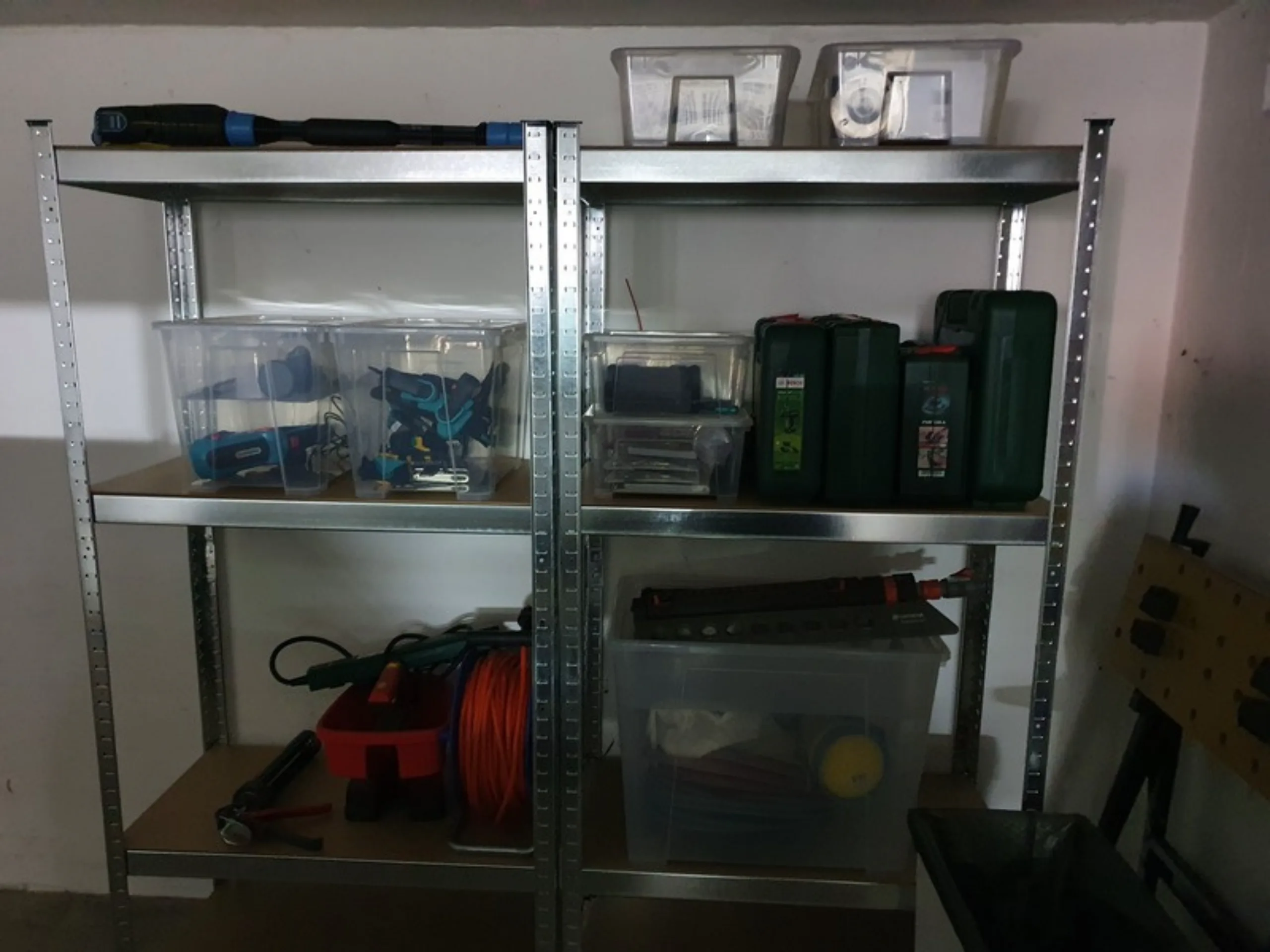 Zwei silberne Schwerlastregale in der Garage, gefüllt mit transparenten Kisten, blauen Akkuschraubern und grünen Werkzeugkoffern