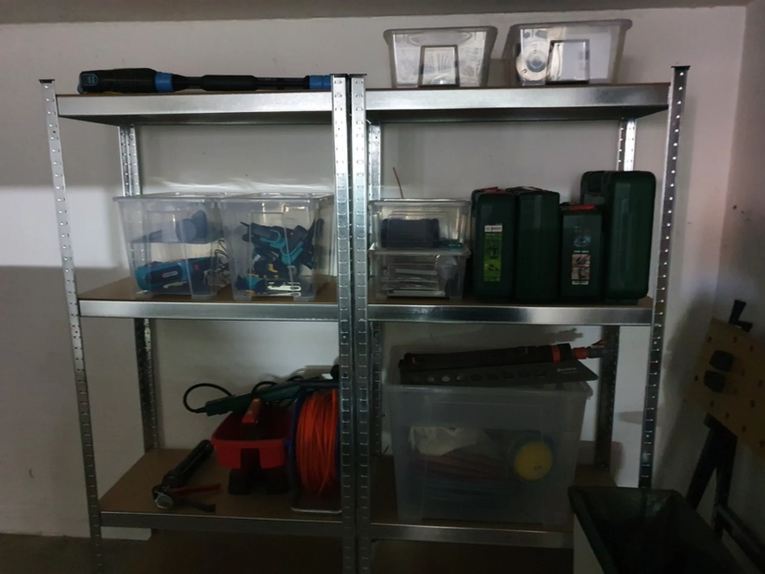 Schwerlastregale in der Garage mit sortierten Kisten, Kabeltrommel und Werkzeugkoffern, rechts eine Lochwand an der Wand