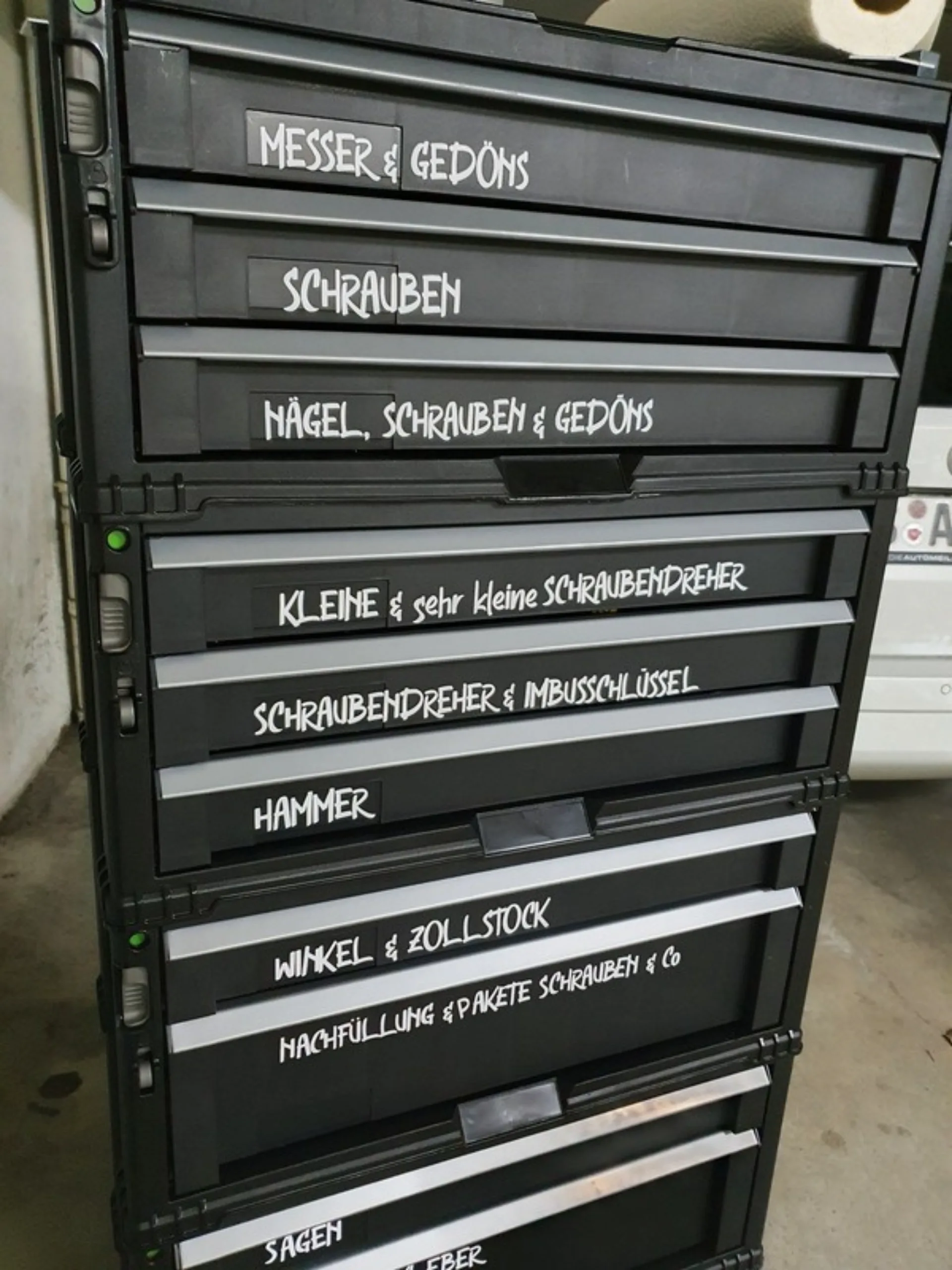 Werkzeugkisten-Turm mit handbeschrifteten Etiketten wie Messer und Gedöns, Schrauben, Hammer, Winkel und Zollstock