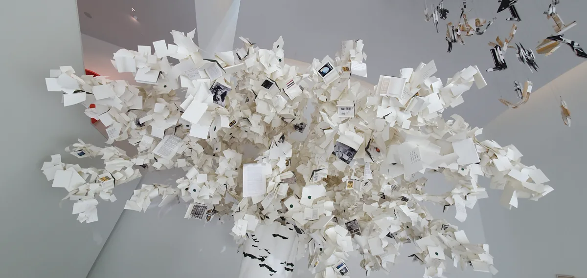 Wolkenartige Deckeninstallation aus hunderten aufgefächerten weißen Buchseiten und Papierschnipseln, dazwischen kleine Fotos und Textfragmente.