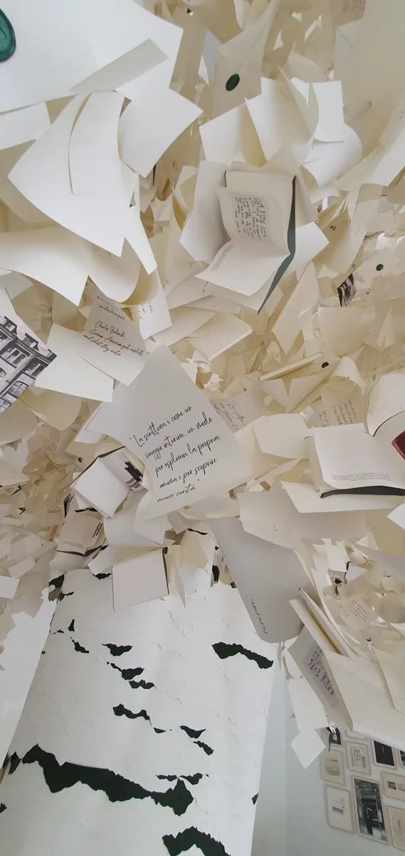 Blick von schräg unten in die üppige Papierkrone aus zahllosen weißen Buchseiten und aufgeklappten Mini-Büchern, unten der birkenartig gemusterte Stamm.