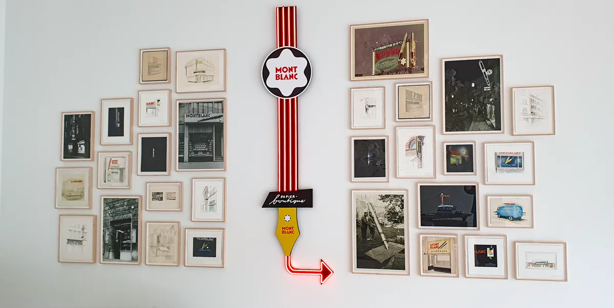 Gerahmte historische Aufnahmen von Montblanc-Läden und Werbeschildern, getrennt durch eine rot leuchtende Neon-Füllfeder mit Stern-Rosette.