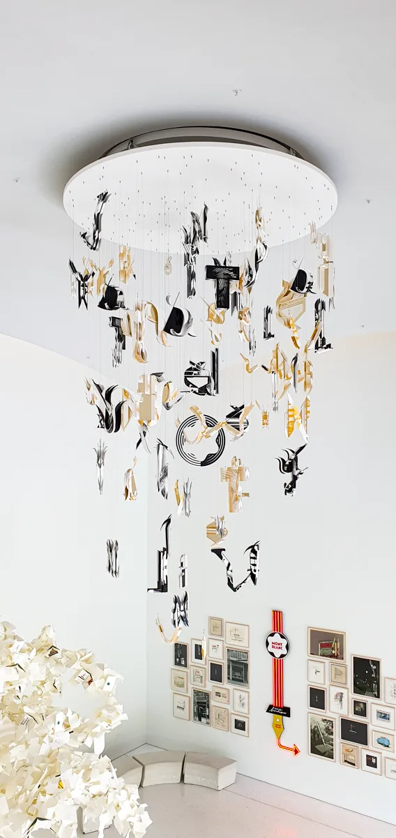 Skulpturale Deckeninstallation aus schwarzen, goldenen und cremefarbenen Formen wie zerbrochene Schriftzeichen, darunter eine kleine Bildergalerie.