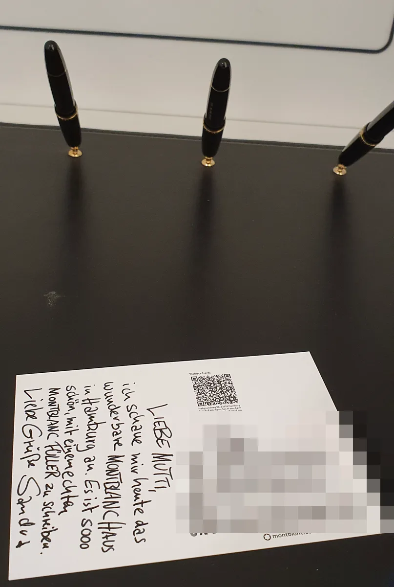 Handgeschriebene Postkarte aus dem Montblanc Haus mit Gruß an die Mutti, davor stecken drei Füllfederhalter zum Testen bereit; die Empfängeradresse ist verpixelt.