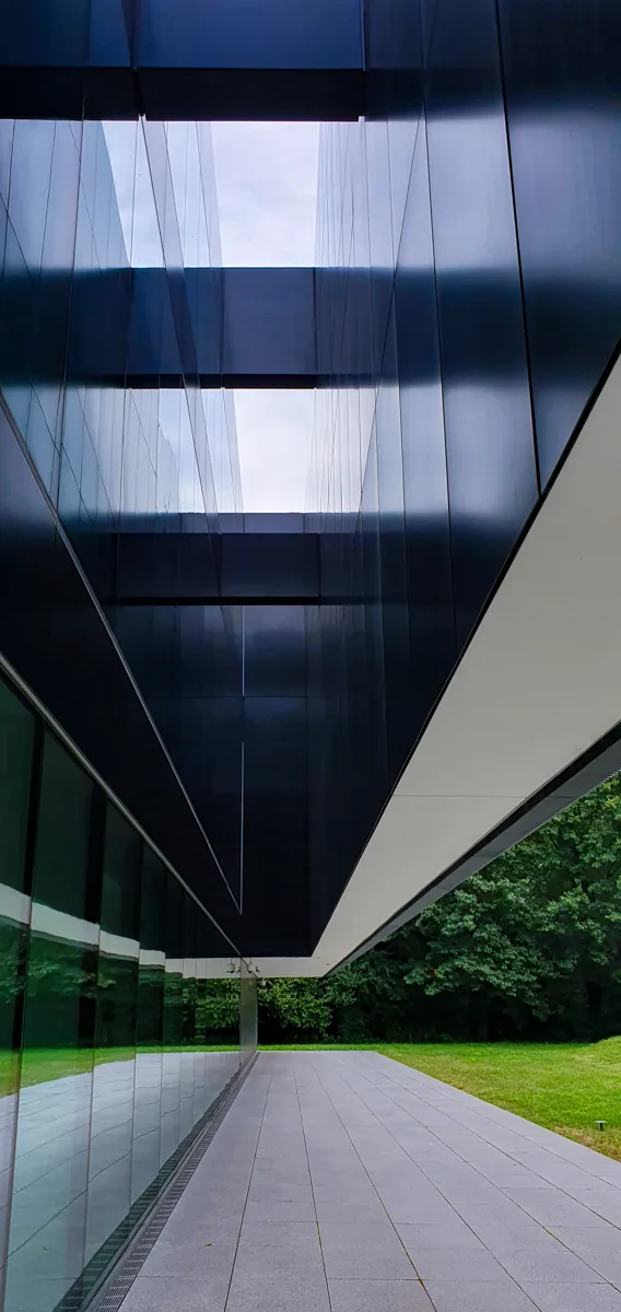 Schmaler Durchgang zwischen den dunkel verspiegelten Glasfassaden des Montblanc Haus, das weiße Vordach zeichnet scharfe geometrische Linien.